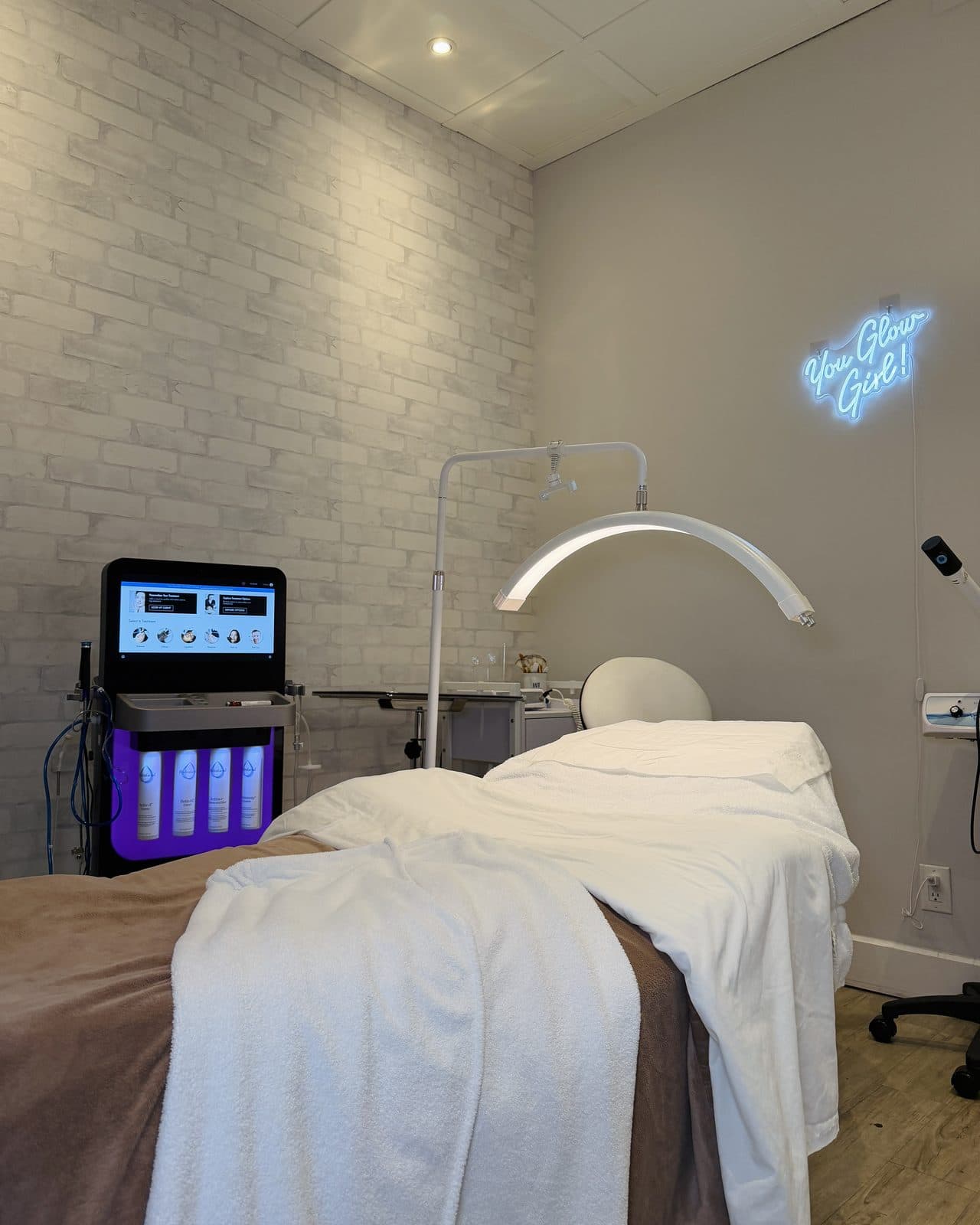 Une salle de soins du visage : un appareil de soin à côté de la table, une lampe DEL en arche et une enseigne au néon