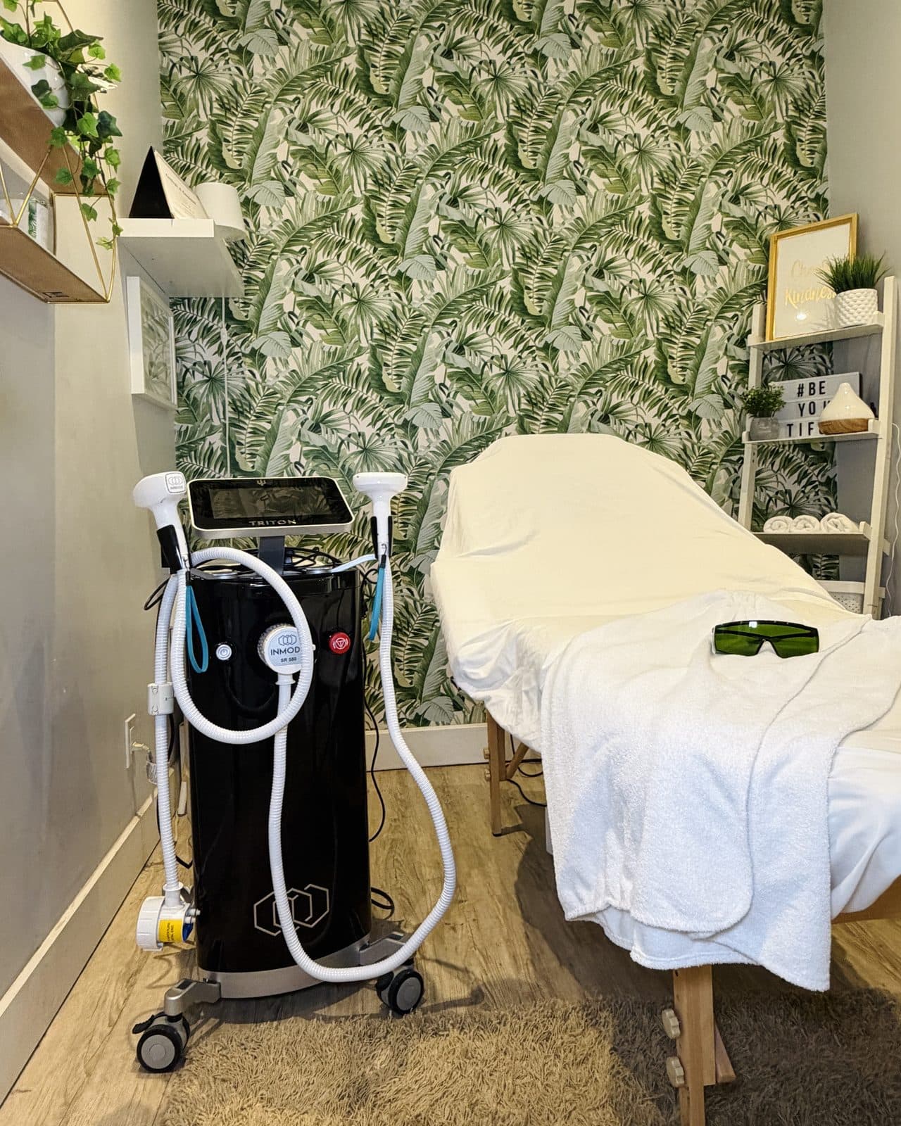 La salle laser : l'appareil laser à côté de la table de soin, devant un papier peint aux feuilles de palmier