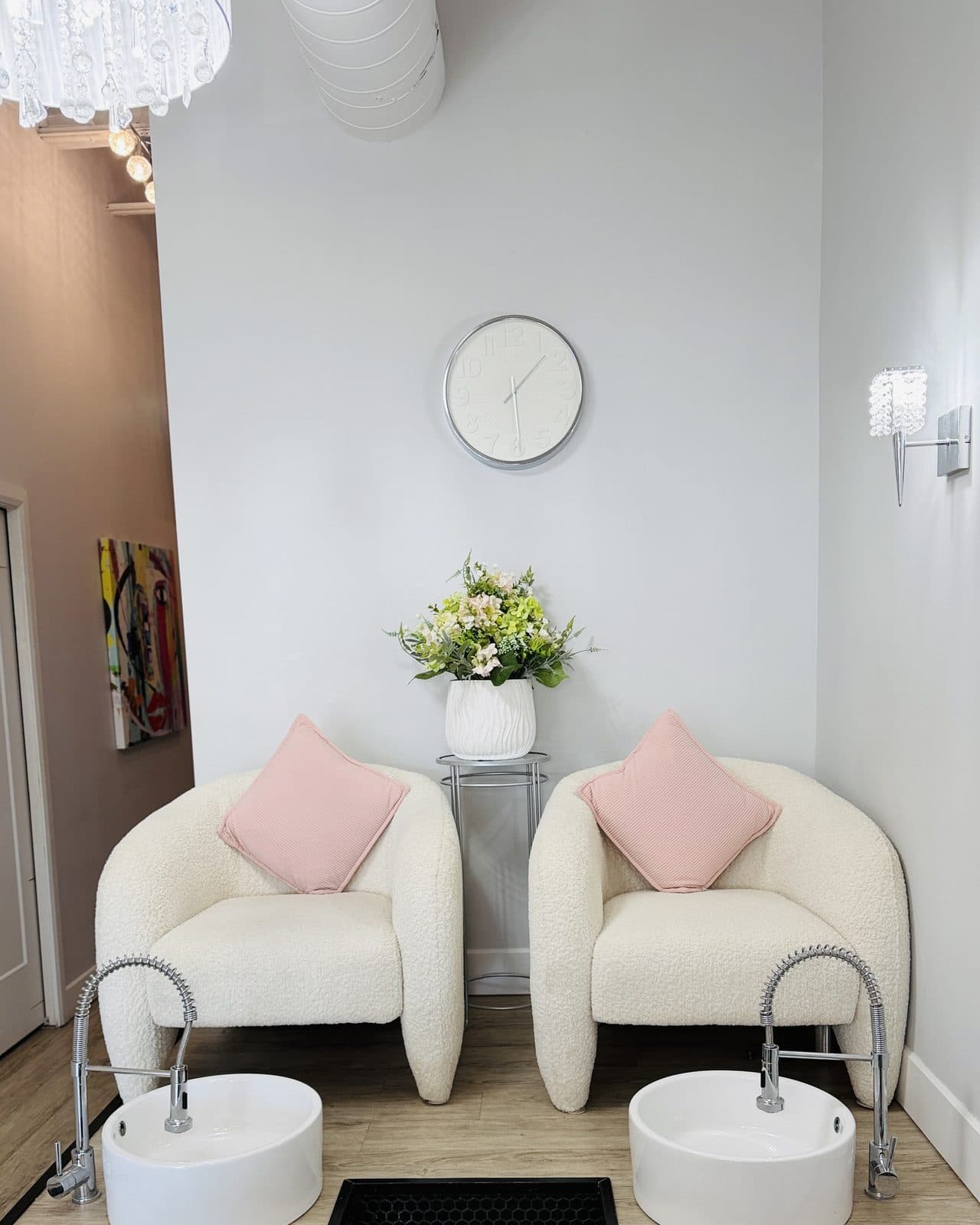 Deux postes de pédicure : des fauteuils bouclés aux coussins roses au-dessus de vasques blanches, sur une estrade en bois