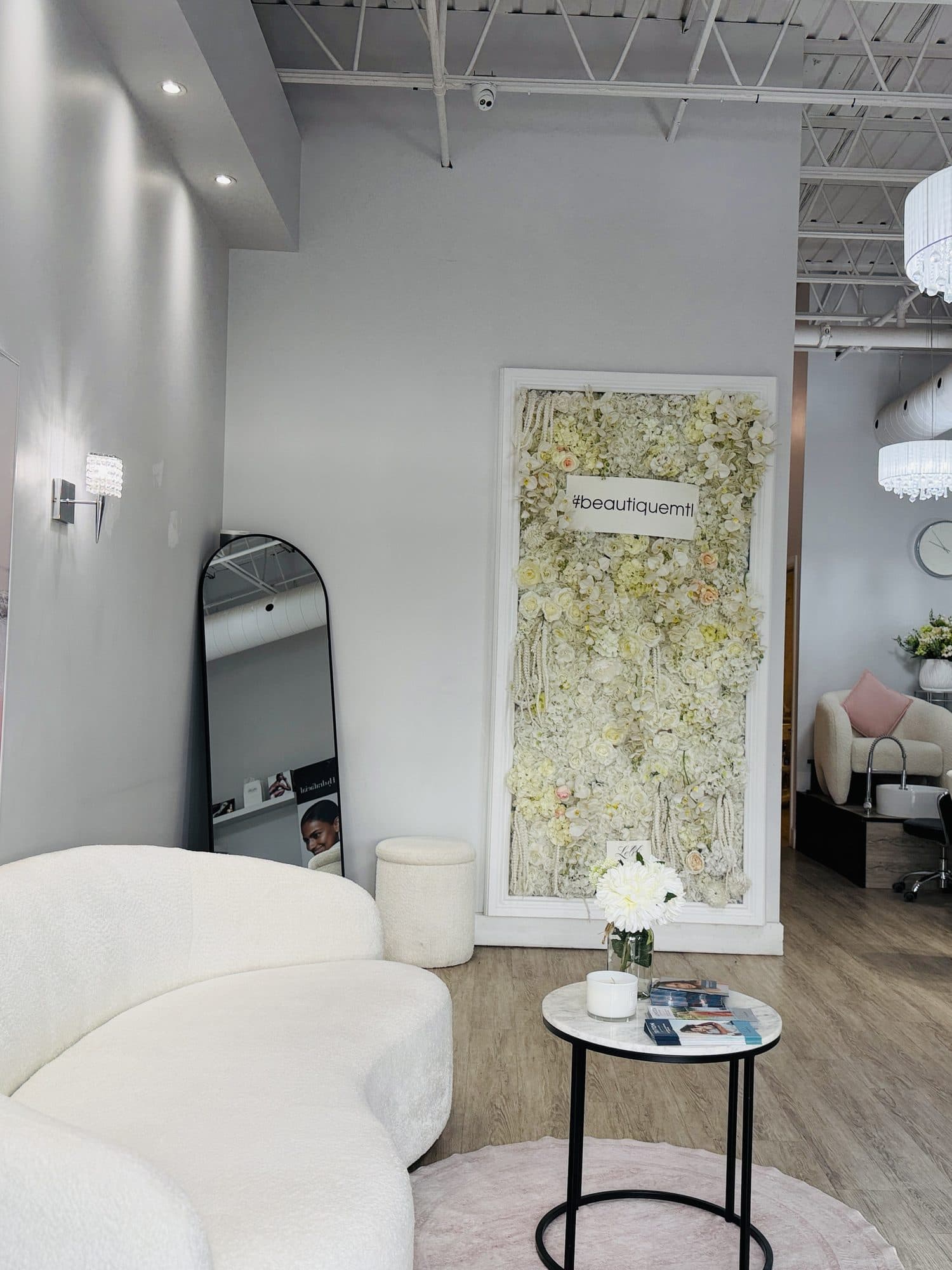 The Beautique salon in Chomedey seen from the entrance: the boucle sofa, the pink seascape canvas, the white flower wall and the nail stations beyond