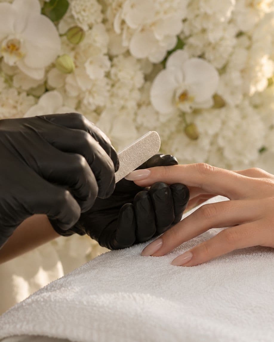 Une technicienne lime un ongle en amande devant le mur de fleurs